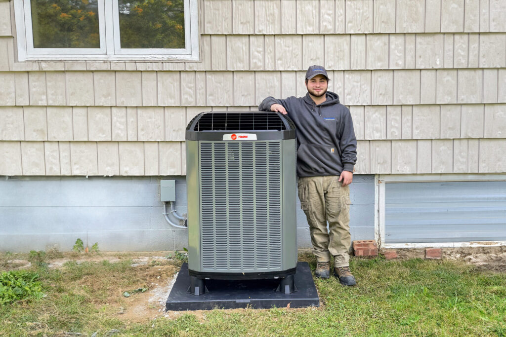 Watkins HVAC tech stands with new Trane XV20i heat pump after replacement job